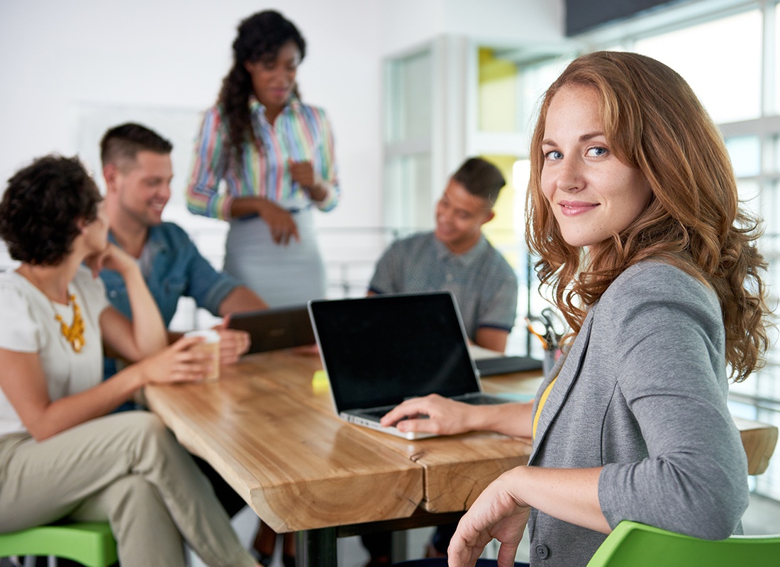 About Our Agency - Woman Looking Back While Using a Laptop in an Office With Her Colleagues